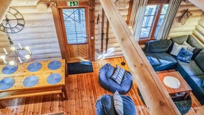 A log cabin interior with a wooden floor, a sofa, a table with a placemat, and a hanging light fixture.