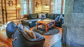 A log cabin interior with a wooden floor, a sofa set, a coffee table, and a stone fireplace.