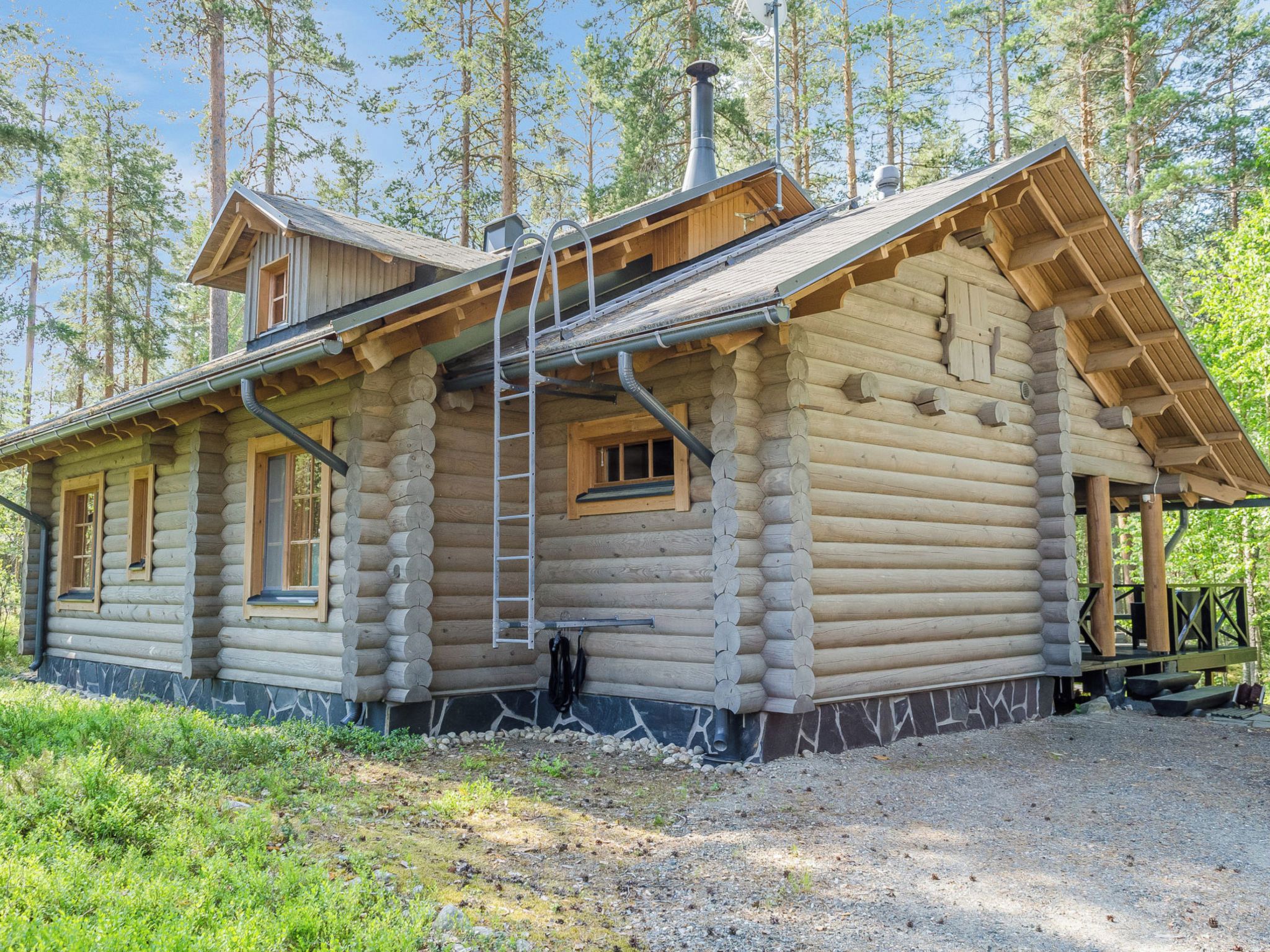Eine Blockhütte mit Veranda, Schornstein und einer Leiter.