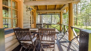 A wooden cabin with a porch featuring two wooden chairs and a table.