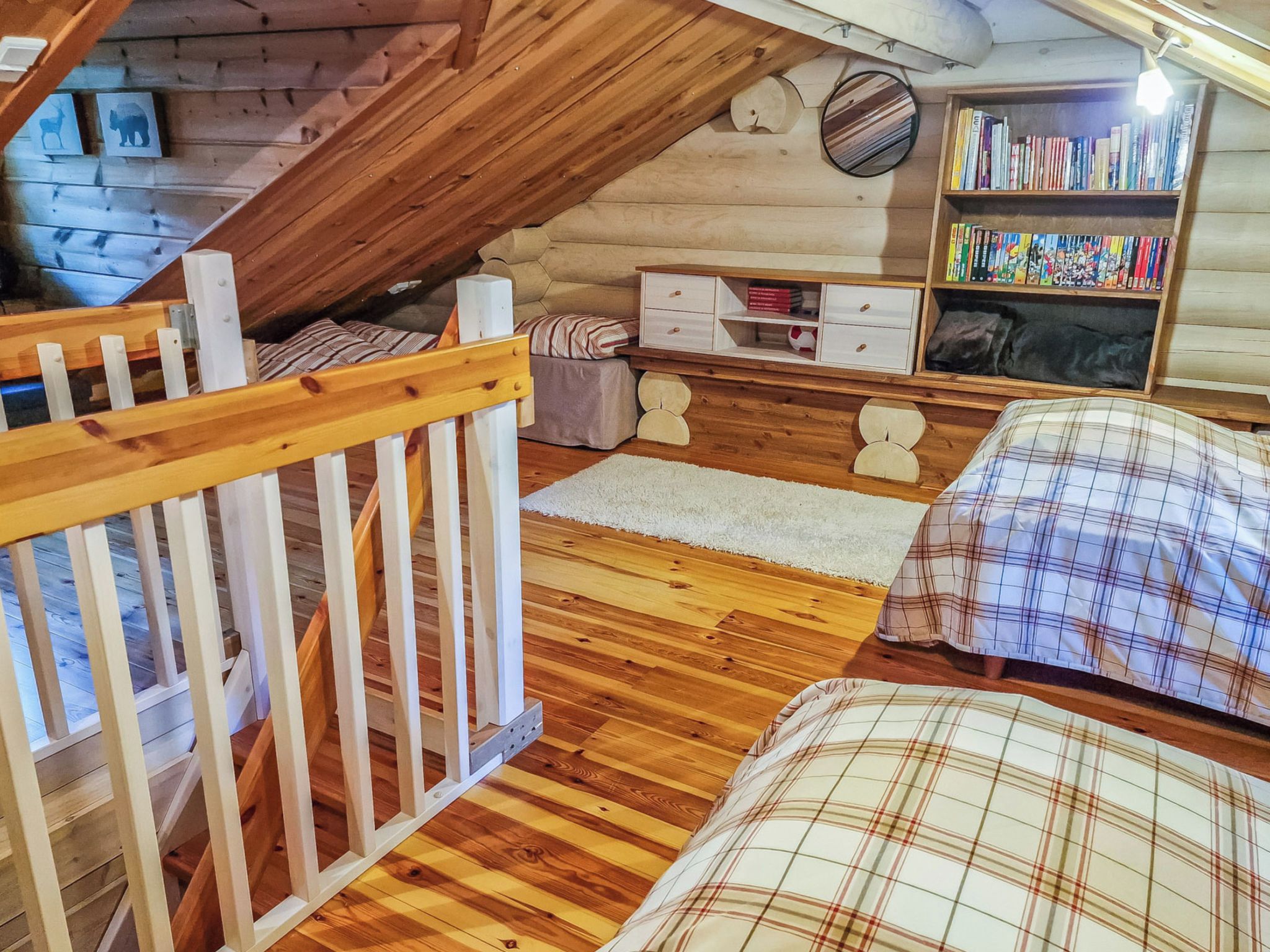 A cozy attic bedroom with a wooden staircase, a bed with plaid bedding, a bookshelf, and a small white dresser.