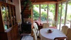 Un cuarto acogedor con un mueble de madera, una chimenea, una mesa de comedor con sillas y un amplio ventanal con vistas a la vegetación.