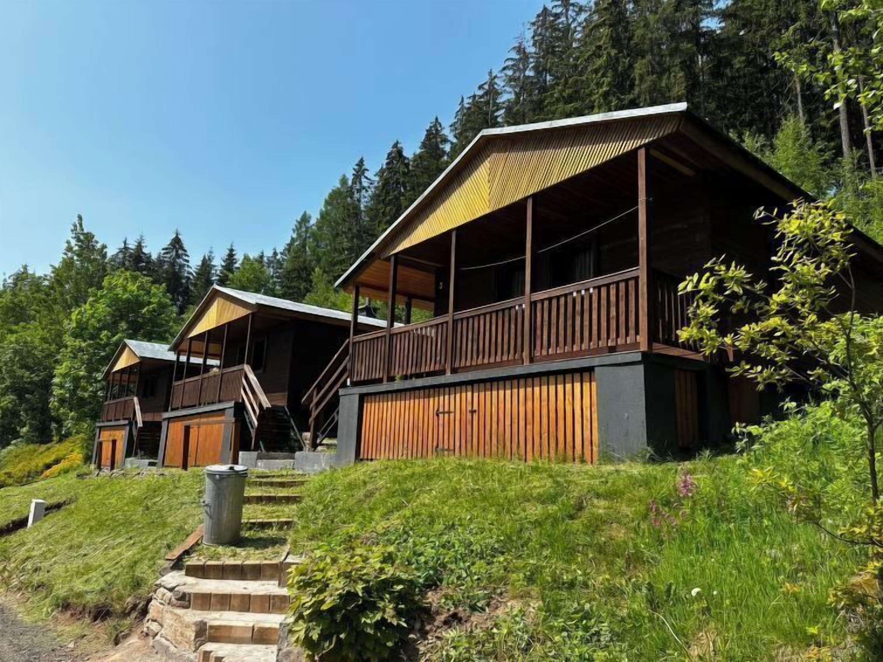 A row of wooden cabins with balconies, set in a forested area with a clear sky.