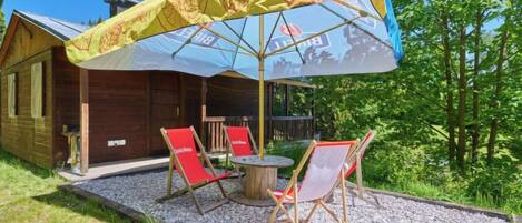 Eine Holzhütte mit überdachter Veranda, auf der zwei rote Klappstühle und ein Tisch stehen.