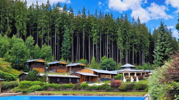 A resort with multiple cabins, a swimming pool, and a forested backdrop.