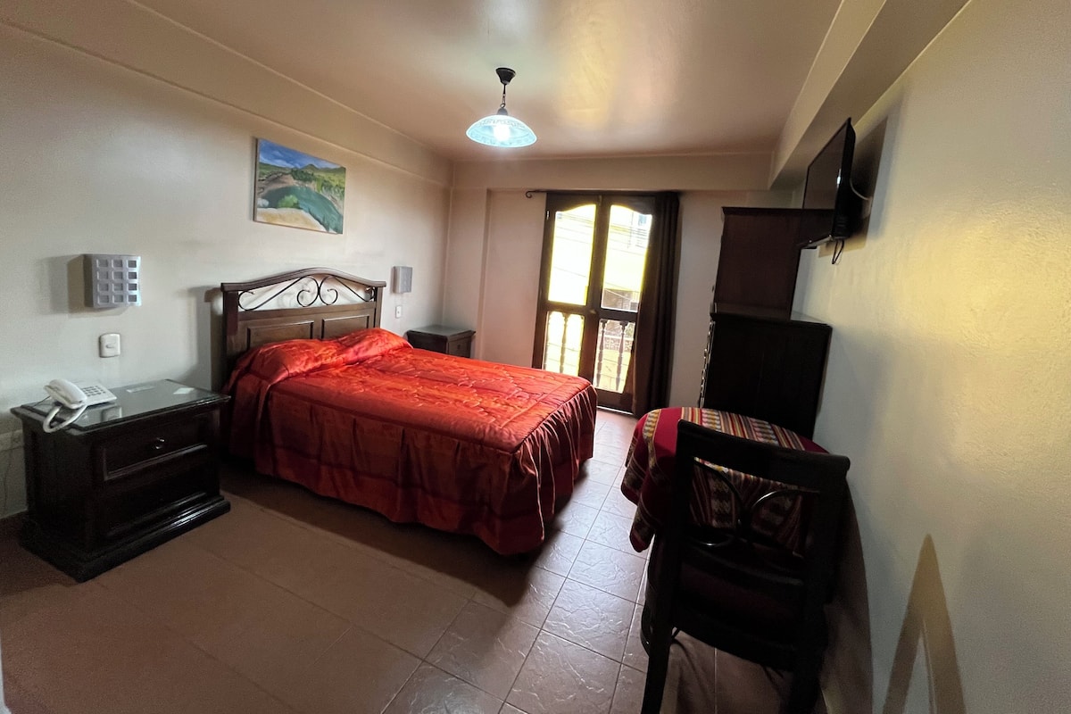 A bedroom with a bed, bedside table, lamp, and a window with curtains.