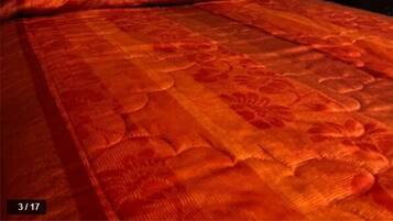Una cama con un edredón rojo estampado, cabecera de metal negro y un cuadro enmarcado sobre la cama.