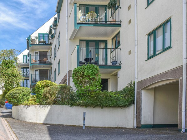 Un immeuble résidentiel à plusieurs étages, doté de balcons, d’un garage et d’un jardin bien entretenu.