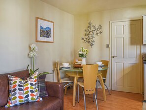 Un coin repas avec une table en verre, des chaises, un vase de fleurs, un tableau encadré et une porte.