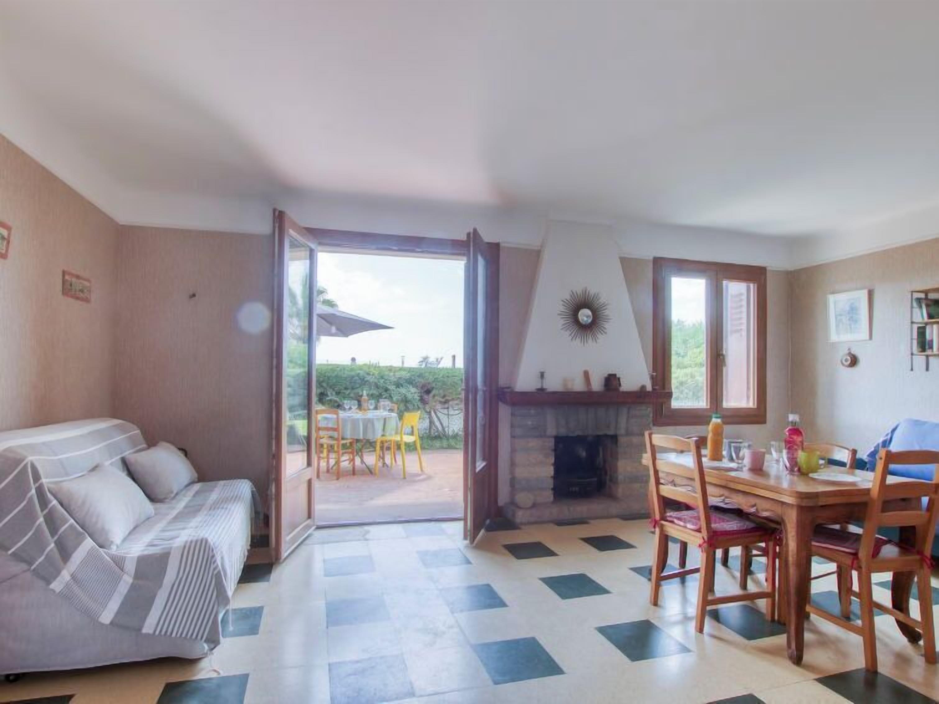 A cozy room with a sofa, a dining table with chairs, a fireplace, and a view through an open door to an outdoor area.