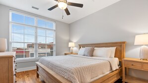 Una camera da letto con un letto grande, una testata imbottita in legno, due comodini con lampade, una ventola a soffitto e una finestra con persiane.