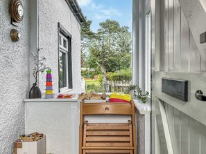 Esterno di una casa bianca con una porta in legno, una finestra, un orologio appeso al muro, un vaso con fiori e una pila di contenitori colorati.