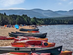 Ein Strand mit aneinandergereihten Kajaks im Sand und Bergen im Hintergrund.