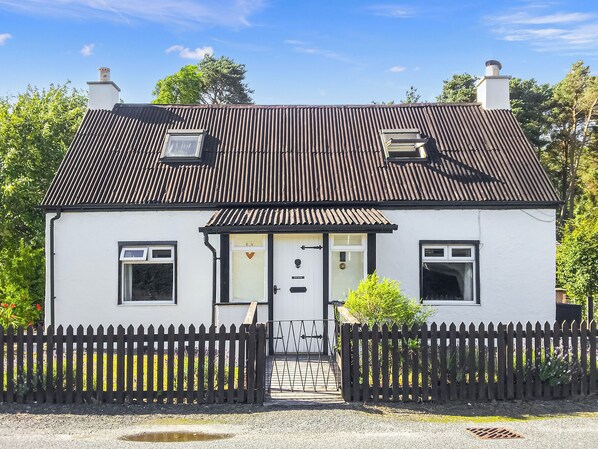 Ein weißes Cottage mit schwarzem Dach, einer Haustür und einem weißen Zaun.