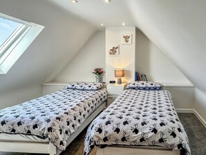Ein Schlafzimmer mit zwei Betten, einem Oberlicht, einem Nachttisch mit Lampe und einer Wanduhr.