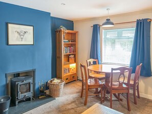 Ein Zimmer mit Kamin, Bücherregal, Esstisch mit Stühlen und einem Vorhangfenster.