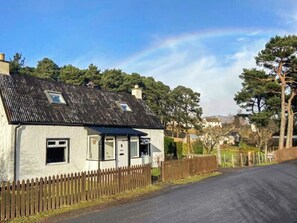 Une petite maison de plain-pied, avec un toit en pente, une clôture en piquets et une allée pavée.