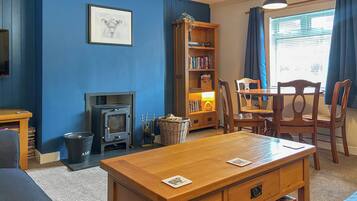 A living room with a fireplace, a bookshelf, a dining table, and a window with curtains.