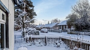 Une rue résidentielle bordée de maisons et d’arbres couverts de neige, avec une clôture en bois et une voiture garée.