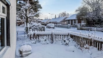 A residential street with snow-covered houses and trees, a wooden fence, and a parked car.