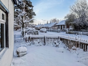 Une rue résidentielle bordée de maisons et d’arbres couverts de neige, avec une clôture en bois et une voiture garée.