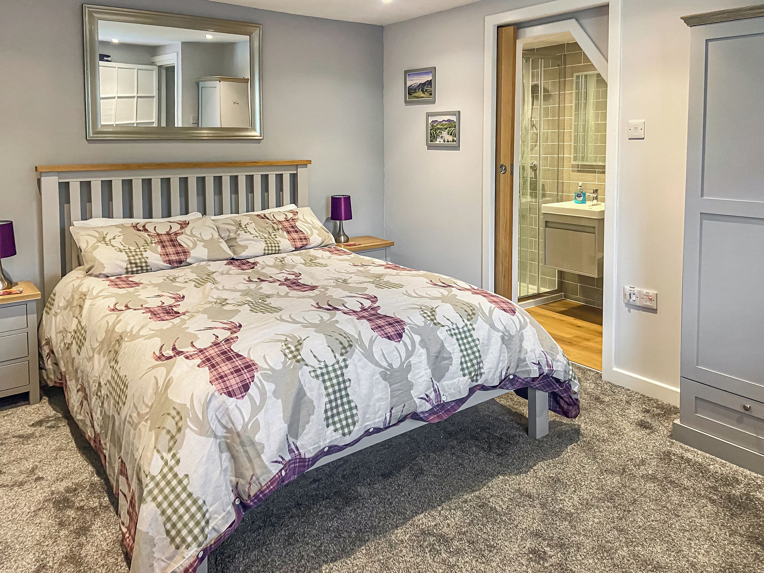 A bedroom with a bed, a nightstand, a bedside lamp, a mirror, and a bathroom visible through an open door.