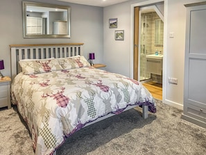 Une chambre à coucher comprenant un lit, une table de chevet, une lampe de chevet, un miroir et une salle de bain visible à travers une porte ouverte.