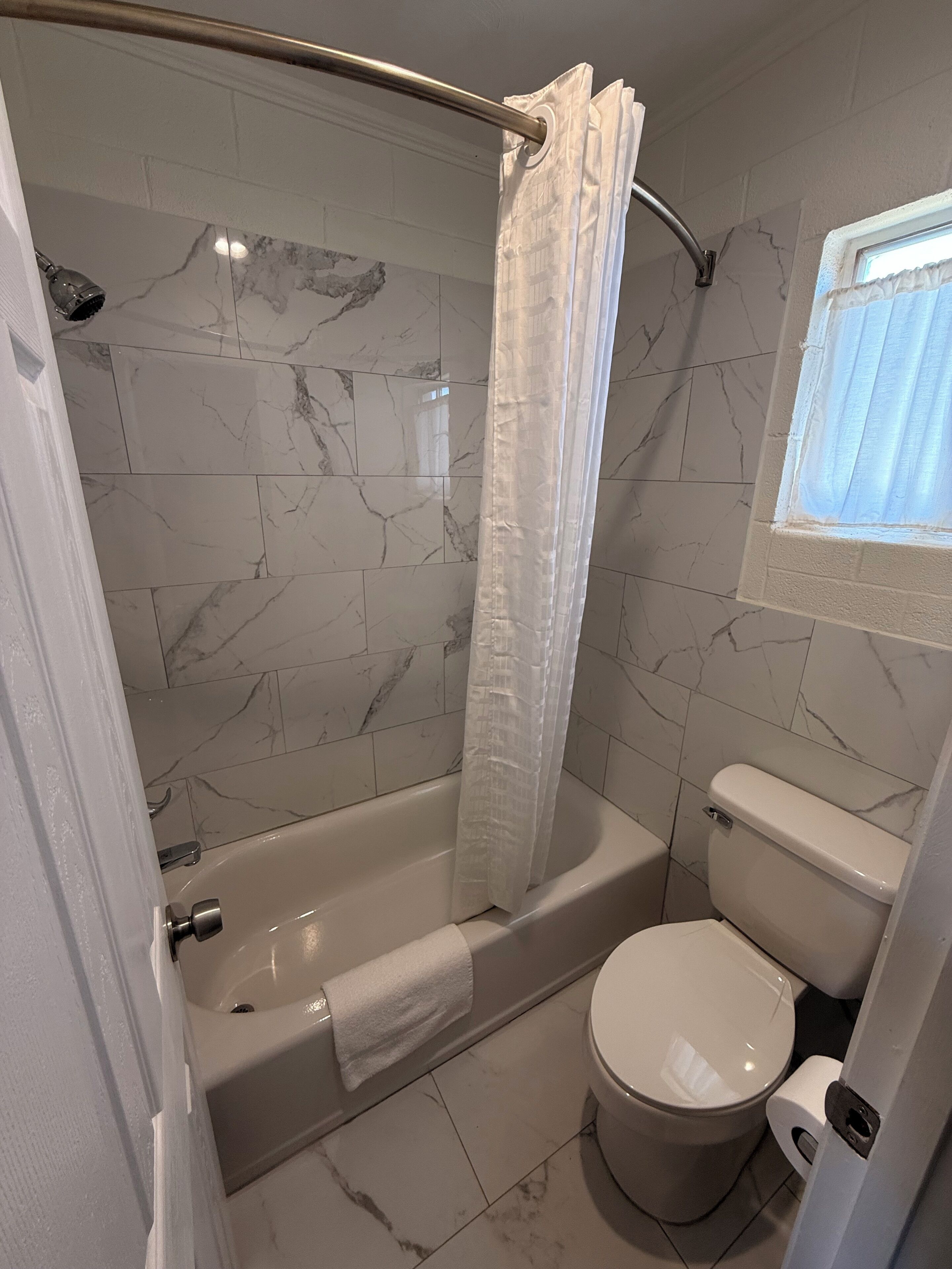 A bathroom with a shower, toilet, and a window.