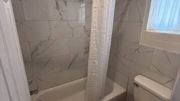 A bathroom with a shower, toilet, and a window.