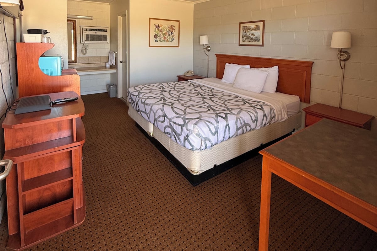 A hotel room with a bed, a desk, a chair, a lamp, and a picture on the wall.