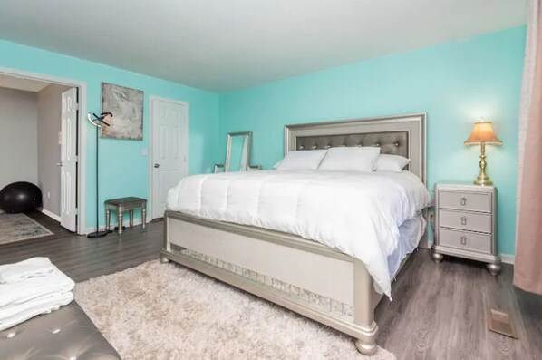 A bedroom with a bed, a nightstand, a lamp, a small stool, and a door.