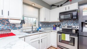 A modern kitchen with white cabinets, a black microwave, a stainless steel refrigerator, and a tiled backsplash. - EverStay Duplex “Suite B” Close to Everything  (charlotte)