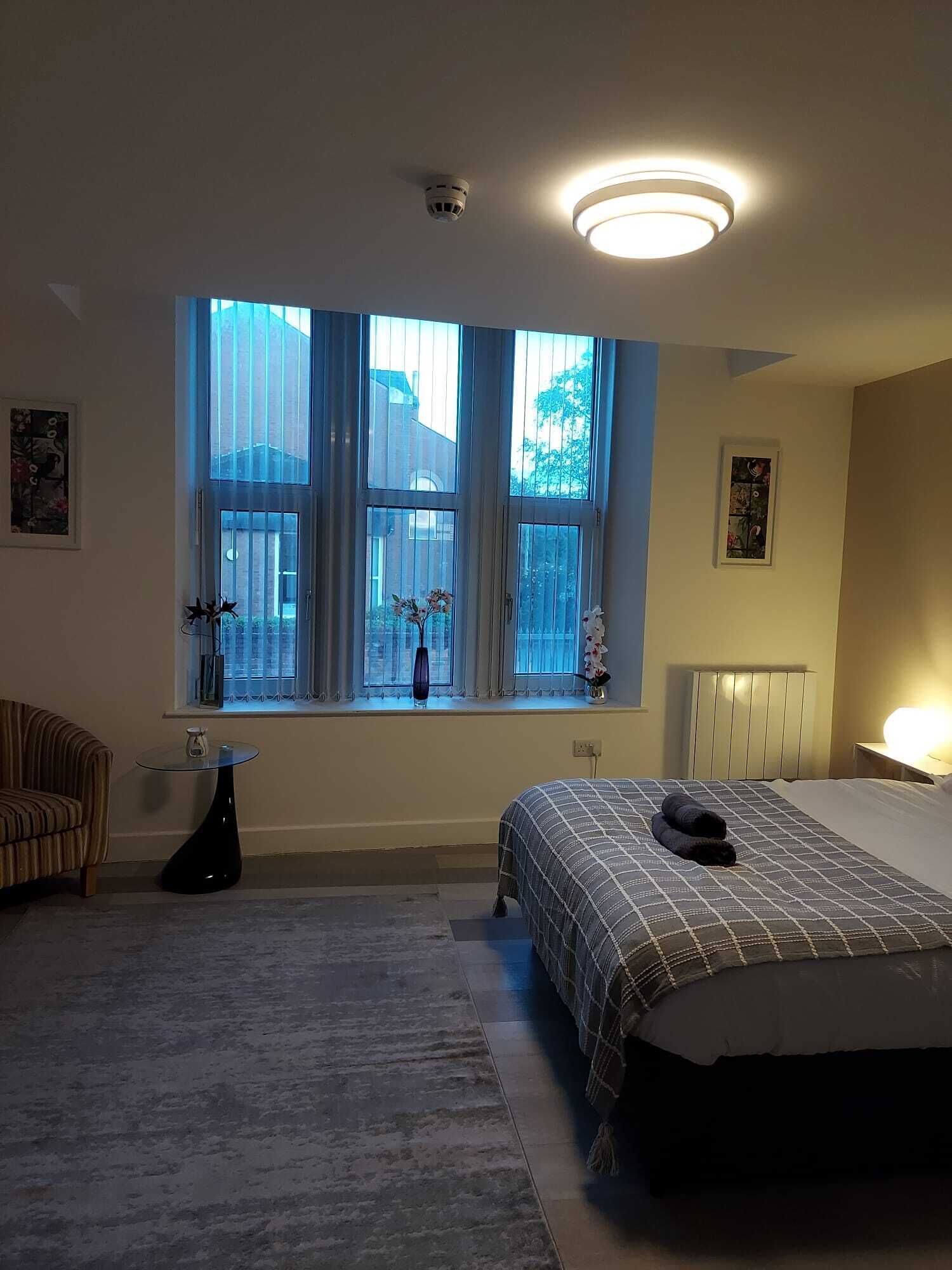 Ein Schlafzimmer mit großem Fenster, einem Bett, einem Sessel und einem kleinen Tisch.