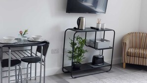 A modern living room with a TV mounted on the wall, a dining area with a table and chairs, and a striped armchair. - Charming 1-bed Studio in Preston (Preston)