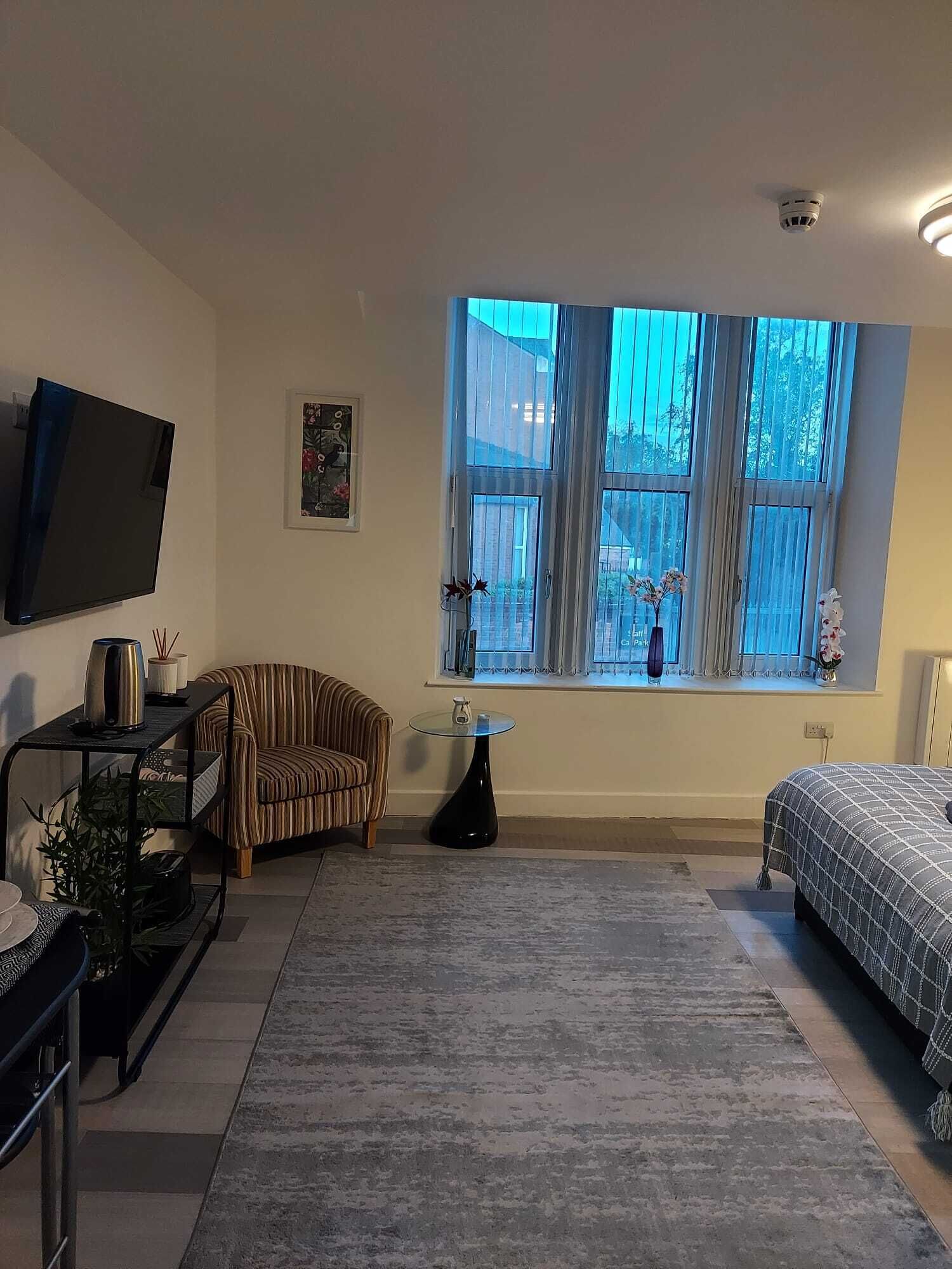A modern bedroom with a large window, a bed, a TV, a striped chair, and a small table with a vase.