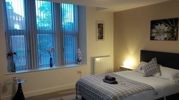 A bedroom with a bed, a bedside table, a window with curtains, a radiator, and a ceiling light. - Charming 1-bed Studio in Preston (Preston)