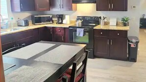 A kitchen with dark wooden cabinets, a microwave, a stove, and a trash can.