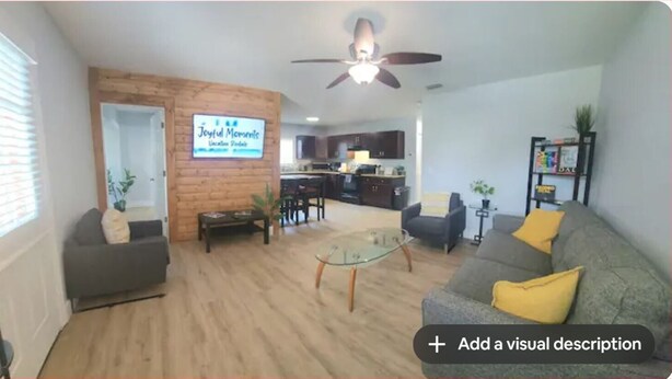 A living room with a wooden accent wall, a glass coffee table, and a ceiling fan.