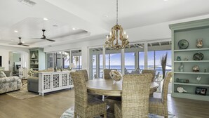 A spacious living room with a round dining table surrounded by wicker chairs, a white cabinet, and a chandelier. - Life Changing Views from this Luxury 3 Bedroom Bayfront Home! (Captiva)