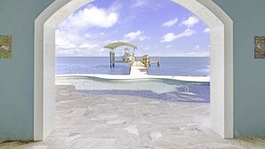 An arched doorway leading to a pool area with a view of the sea and a covered seating area. - Life Changing Views from this Luxury 3 Bedroom Bayfront Home! (Captiva)