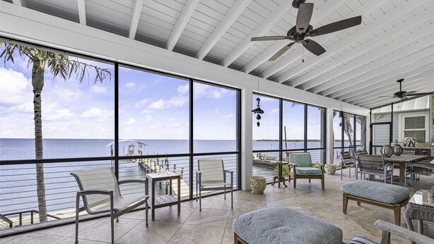 A spacious balcony with large windows overlooking the sea, furnished with chairs and a table. - Life Changing Views from this Luxury 3 Bedroom Bayfront Home! (Captiva)