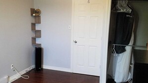 Une pièce avec une porte blanche, un porte-manteau sur lequel sont suspendus des vêtements, un haut-parleur noir et une étagère murale ornée d’objets décoratifs.