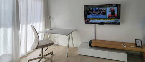 A modern office space with a desk, chair, and a mounted television displaying a sports program.