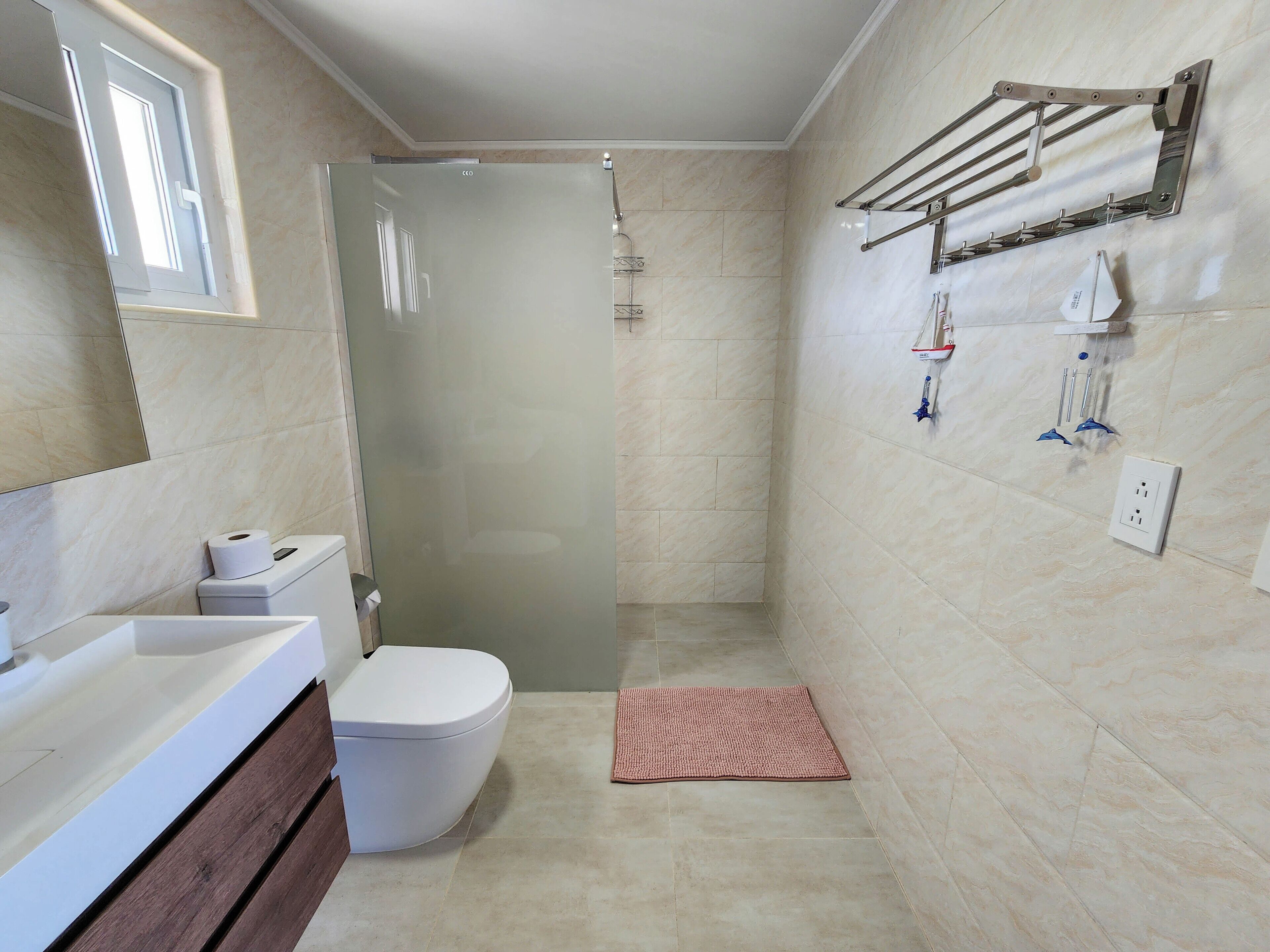 Un baño moderno con ducha envuelta en vidrio, inodoro blanco, tocador con espejo y toallero en la pared.