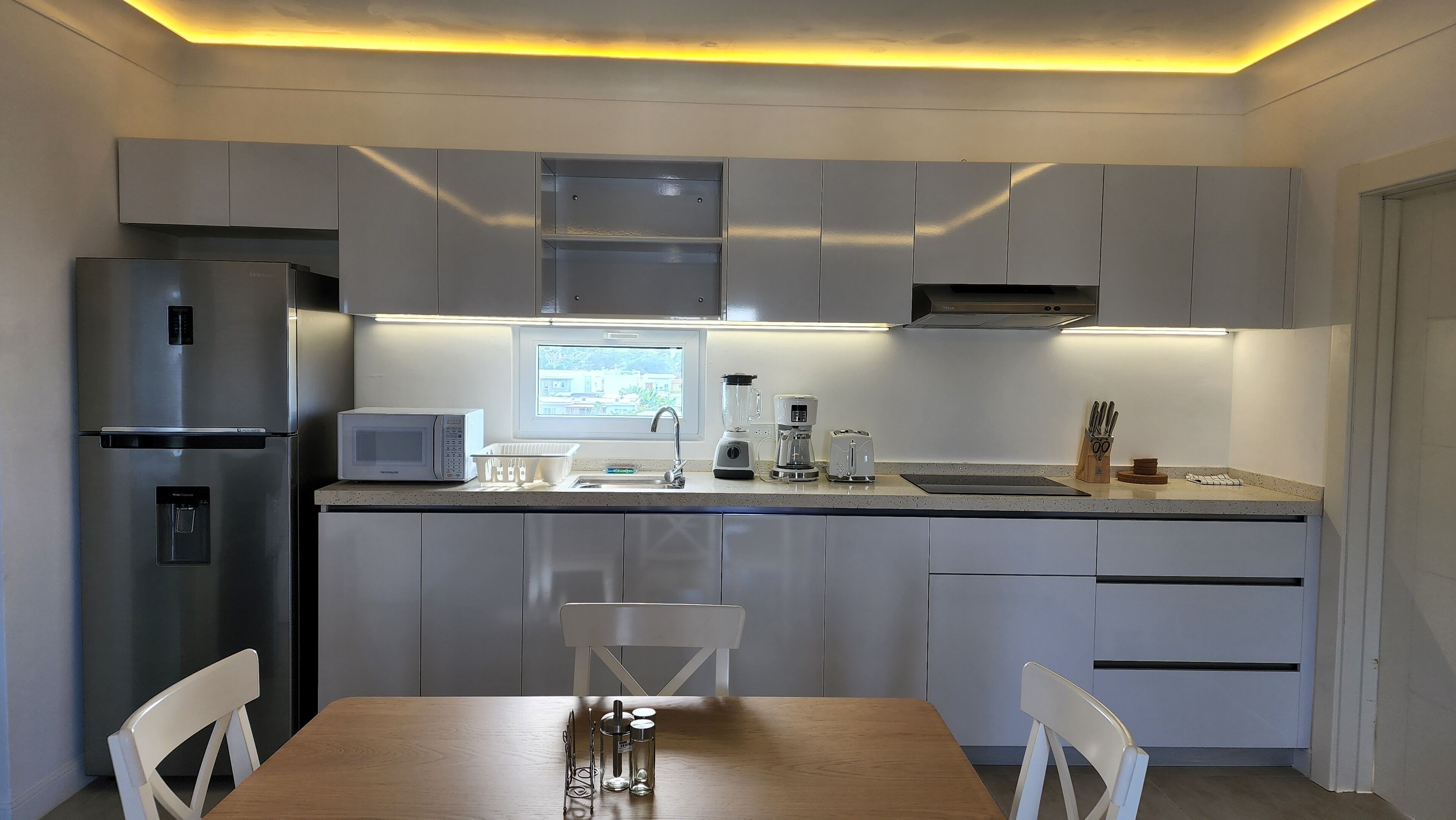 Una cocina moderna con electrodomésticos de acero inoxidable, una ventana y un comedor con mesa y sillas de madera.
