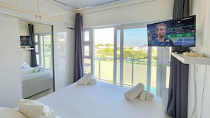 Hotellihuone, jossa on suuri sänky, televisio ja parveke, jolta on näkymä.