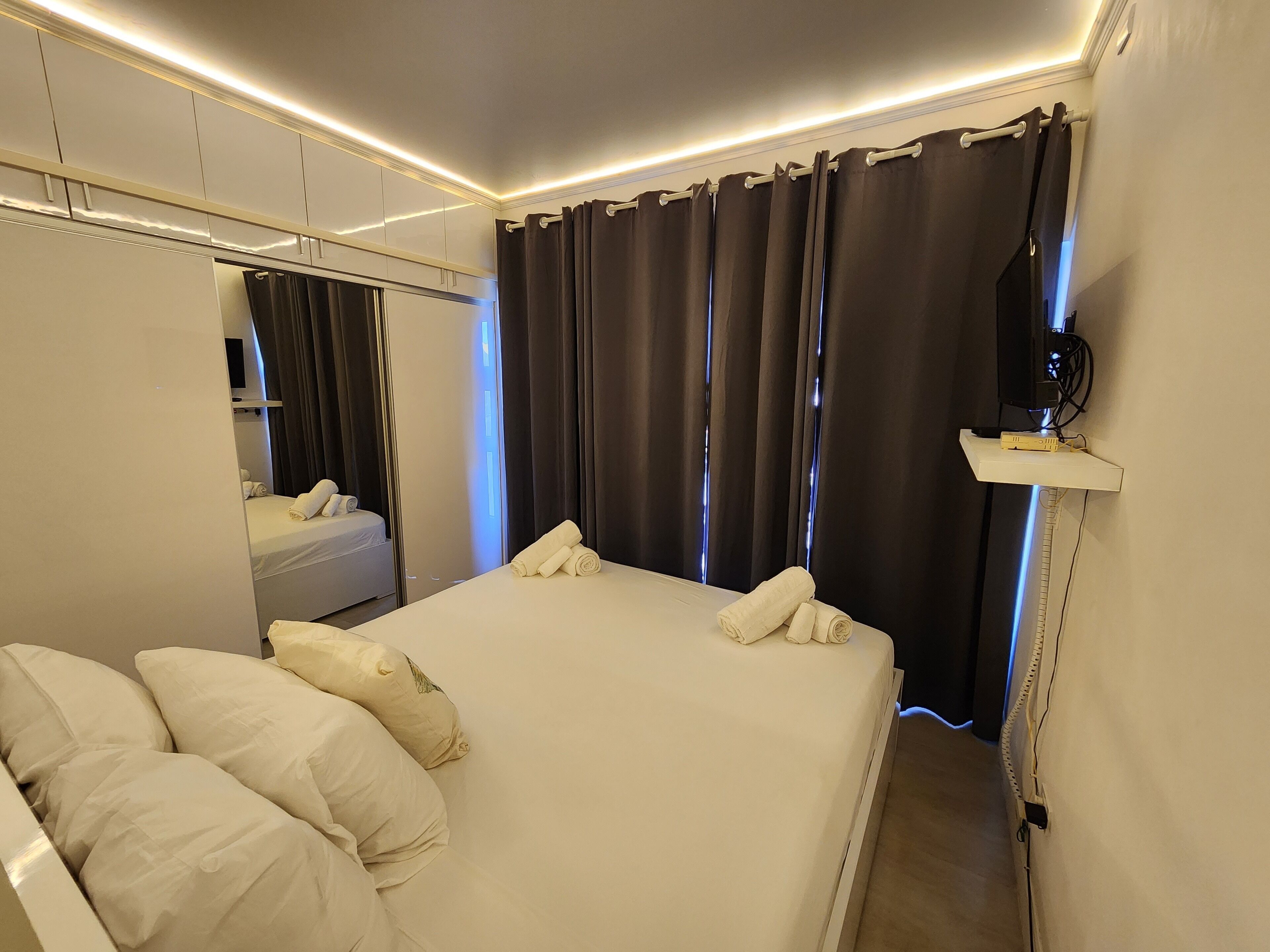 Une chambre d’hôtel avec un lit, des oreillers, un miroir, une télévision et un rideau.