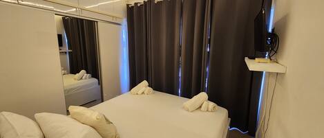 Una habitación de hotel con una cama, almohadas, un espejo, un televisor y una cortina.