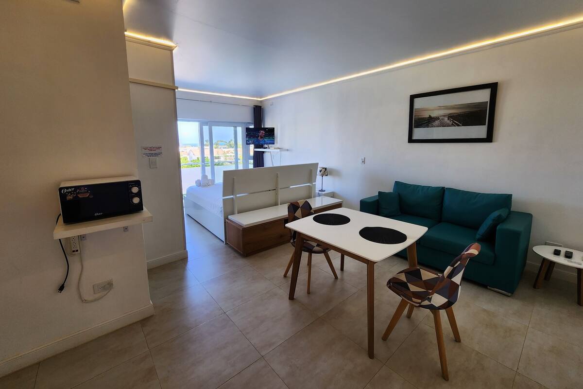 Een moderne woonkamer met een bank, een tafel en een televisie. Er is een balkon met uitzicht op het strand.