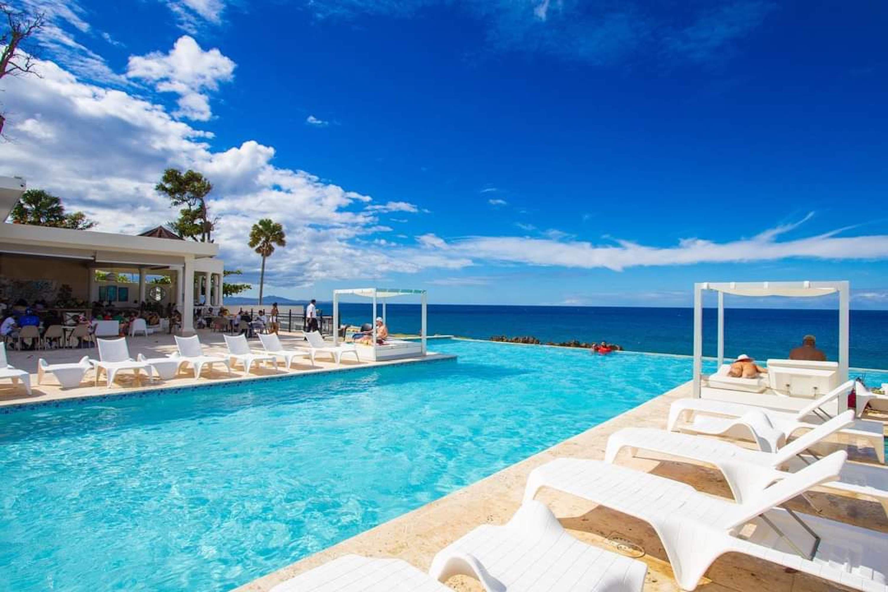 A pool area with lounge chairs and a view of the ocean.
